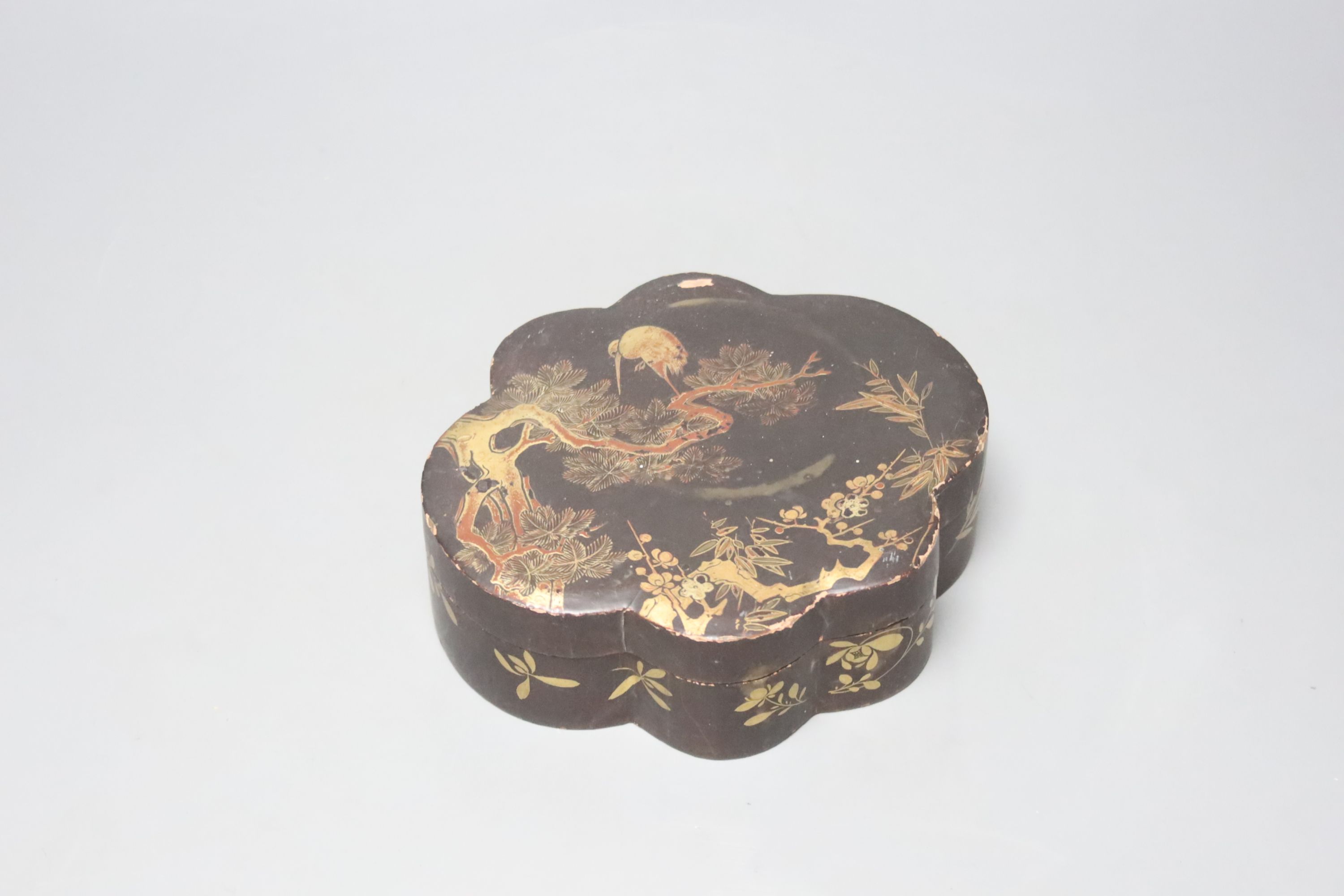 A Japanese black-lacquered box and cover, of shaped oval form, the top decorated in red and gilt with a stork on a branch, prunus, etc, L 16.5cm